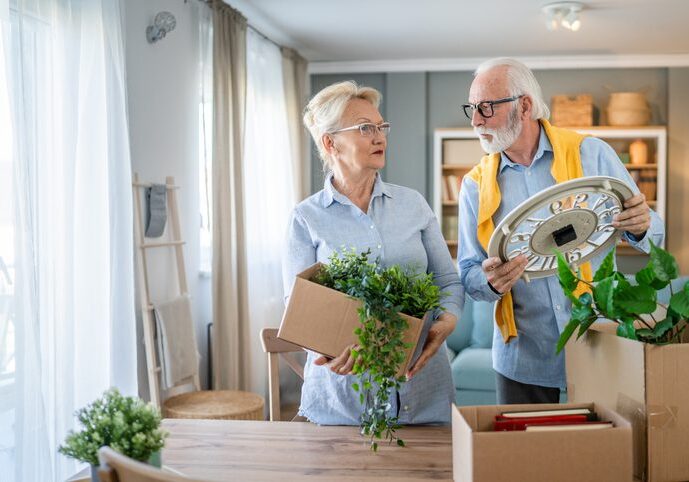 family senior couple man woman husband and wife pensioner grandfather grandmother moving in new apartment taking their stuff belongings and plants in or out of boxes packing or unpacking real people