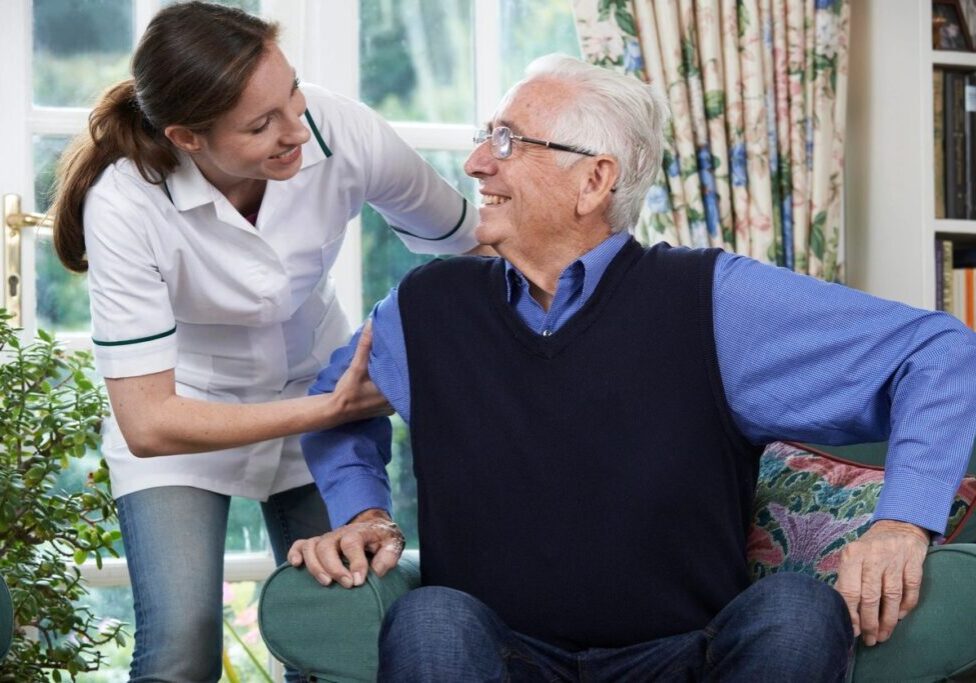 A woman is helping an older man sit in his chair.